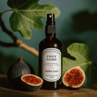 Bottle of 'Figue Noire' perfume by Atelier Louis with figs and leaves in the background